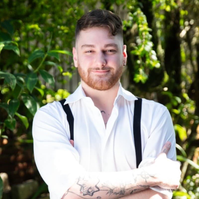 a man with tattoos standing in front of trees