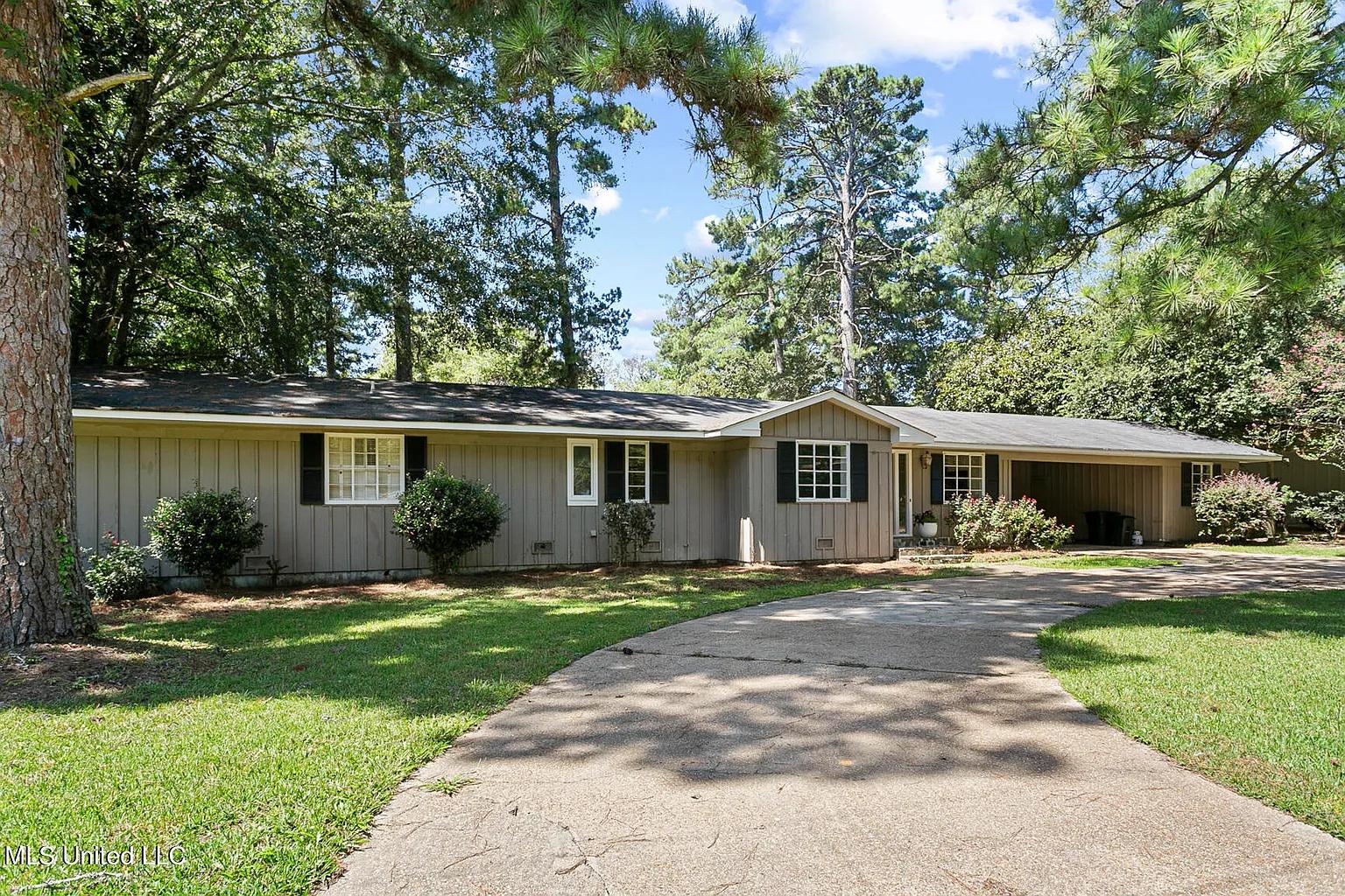 a home in the woods with a driveway and trees